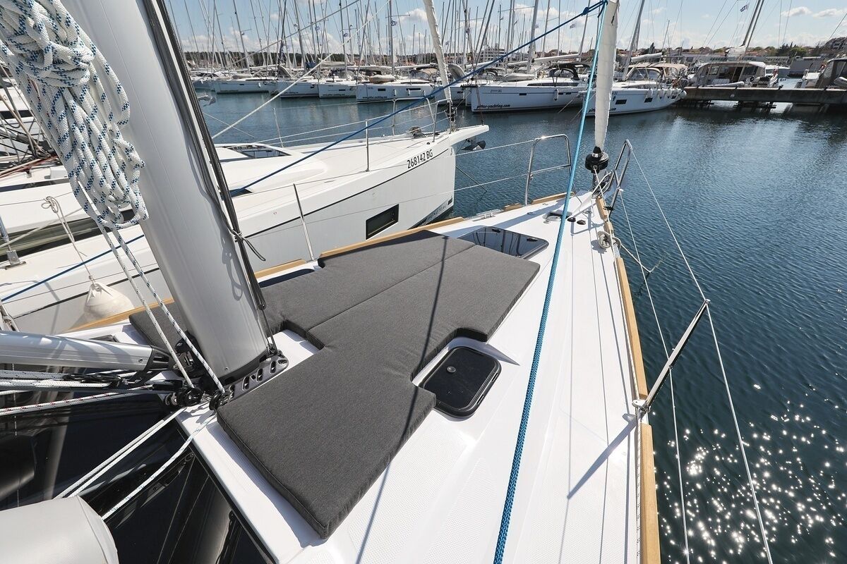 A sailboat deck with a cushioned seating area, a mast, and multiple boats docked in the background.