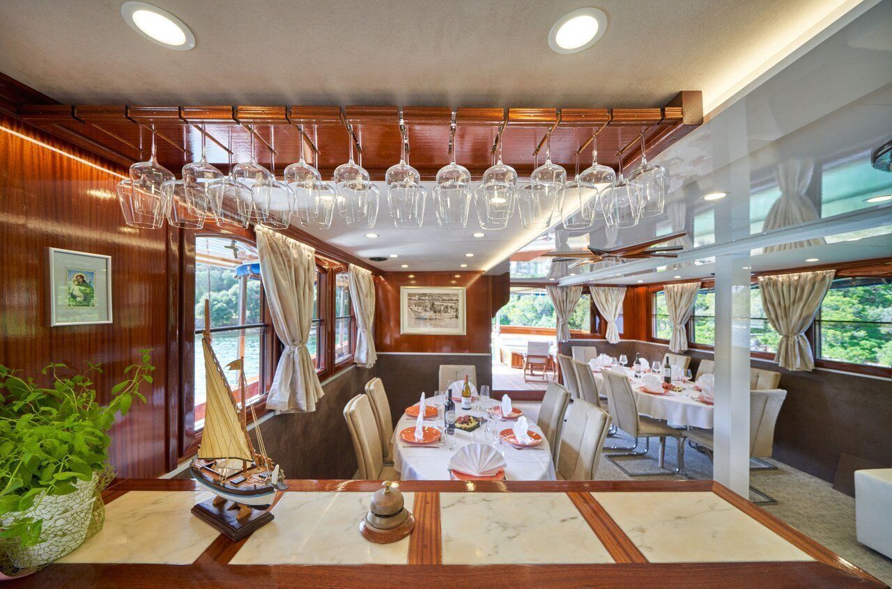 A dining area with tables set for service, a ship model on the table, and a view of the outdoors through large windows.