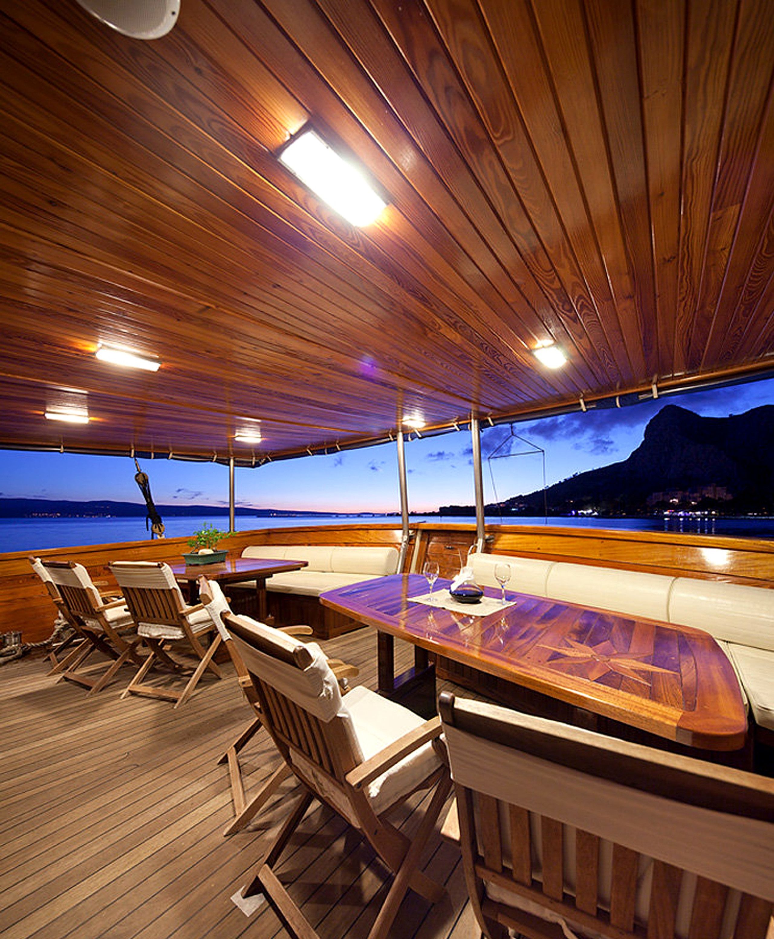 Une terrasse extérieure avec un plancher en bois, des sièges et une vue sur la mer au crépuscule.