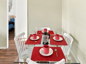 Una mesa de comedor con cuatro sillas, individuales rojos y tazas rosas.