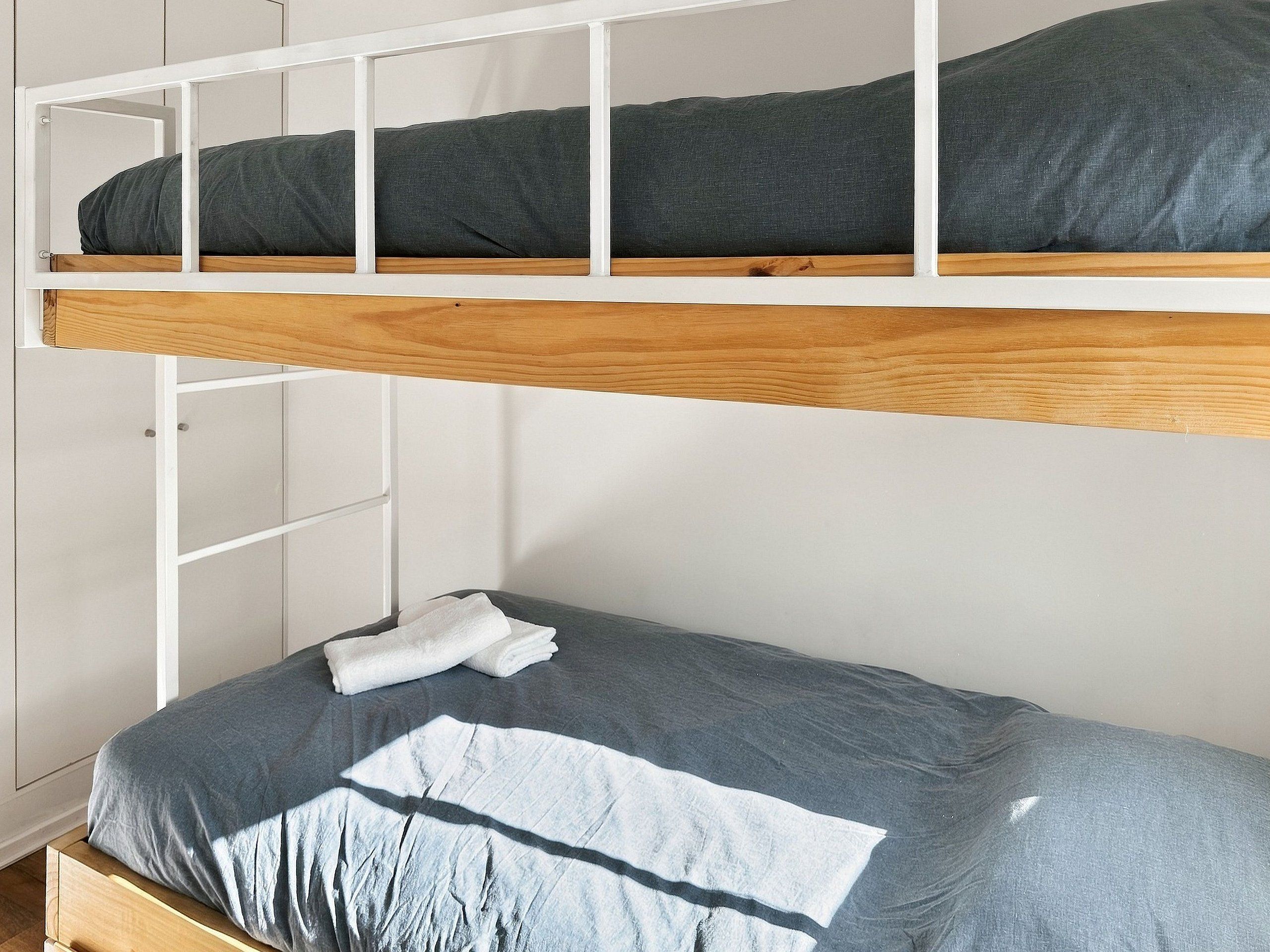 A bunk bed with a wooden frame and a lower single bed.