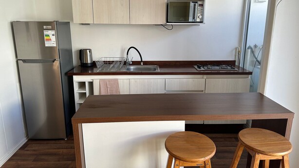 A modern kitchen with a built-in microwave, stainless steel refrigerator, and a wooden island with stools. - Oceana Suites Pucón vista al volcán (Pucon)