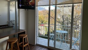 A room with a large window, a TV mounted on the wall, a kitchen area, and a balcony with outdoor furniture. - Oceana Suites Pucón vista al volcán (Pucon)