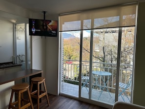 A room with a large window, a TV mounted on the wall, a kitchen area, and a balcony with outdoor furniture. - Oceana Suites Pucón vista al volcán (Pucon)
