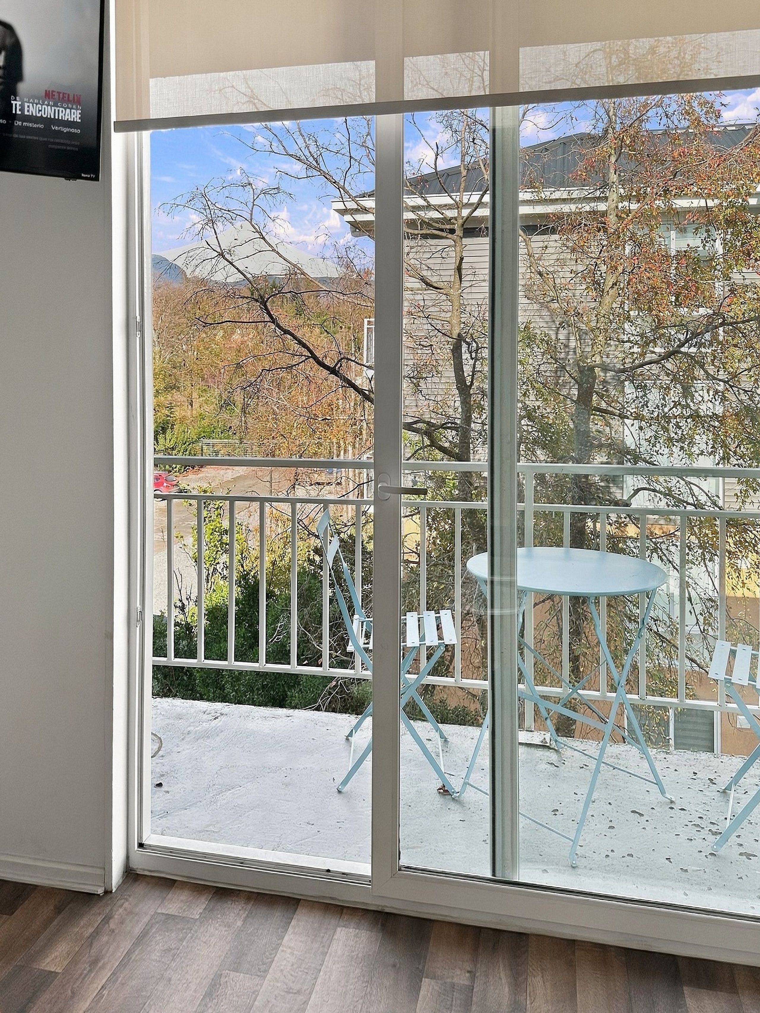 Une pièce dotée d’une porte-fenêtre coulissante donnant sur un balcon extérieur avec une table et des chaises.