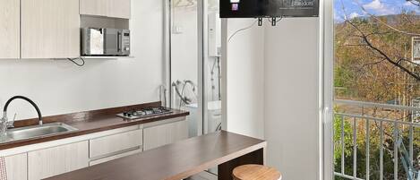 A modern kitchen with a flat-screen TV mounted above the counter, a gas stove, and a sink. There are two wooden stools at the counter.