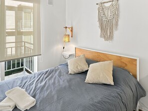 Une chambre à coucher avec un lit, des oreillers, une lampe de chevet et une décoration murale en macramé.