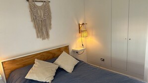 A bed with a wooden headboard, two pillows, a wall-mounted macrame piece, and a wall-mounted lamp. - Oceana Suites Pucón vista al volcán (Pucon)