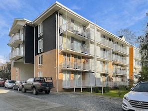 Um edifício residencial com vários andares, varandas, área de estacionamento com carros e céu claro.