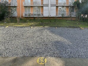 Un immeuble à plusieurs étages doté de balcons, une allée gravillonnée et un dos d’âne jaune.