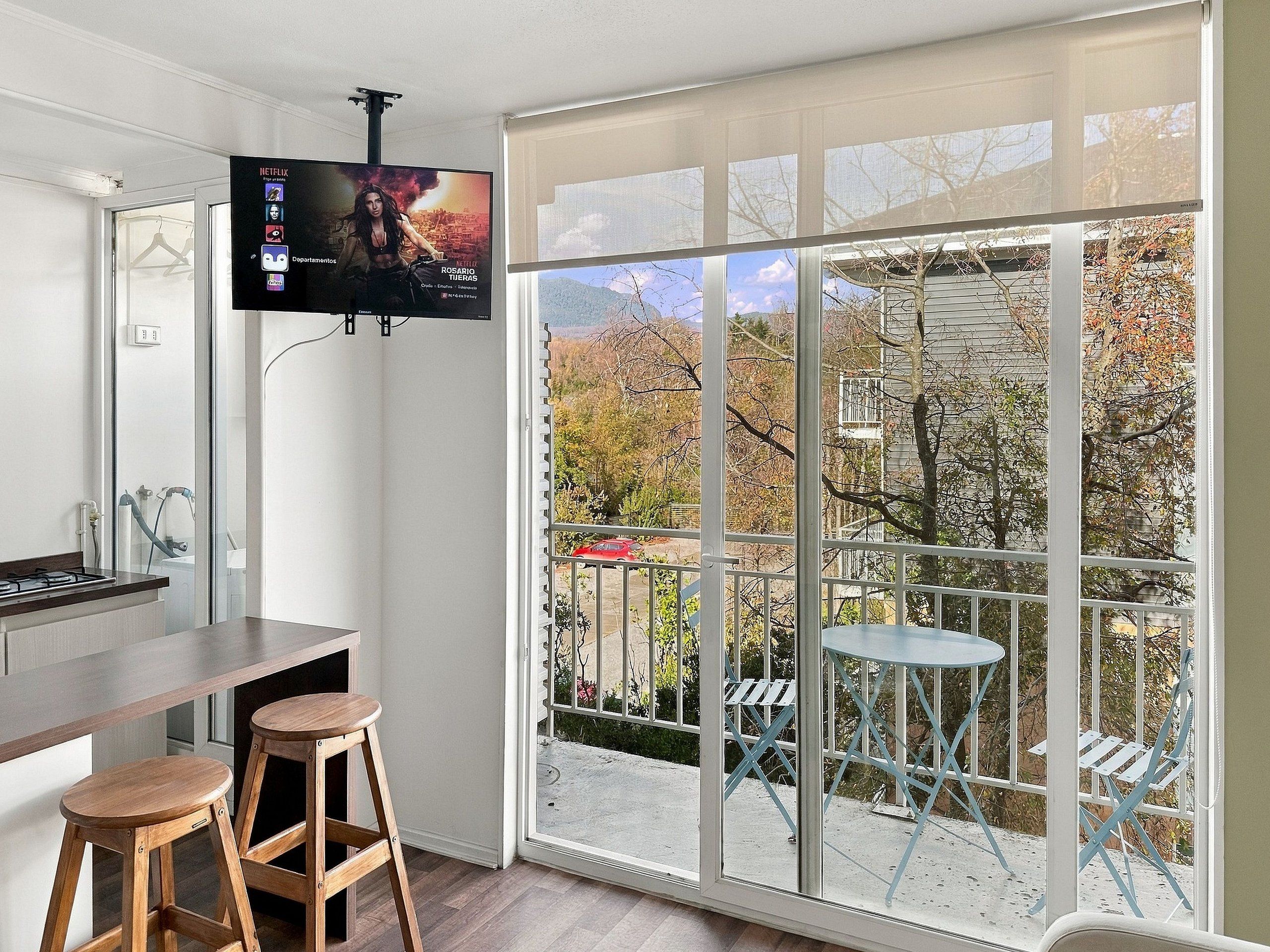 A modern kitchen with a TV mounted above the counter, a sliding glass door leading to an outdoor patio with chairs and a table.