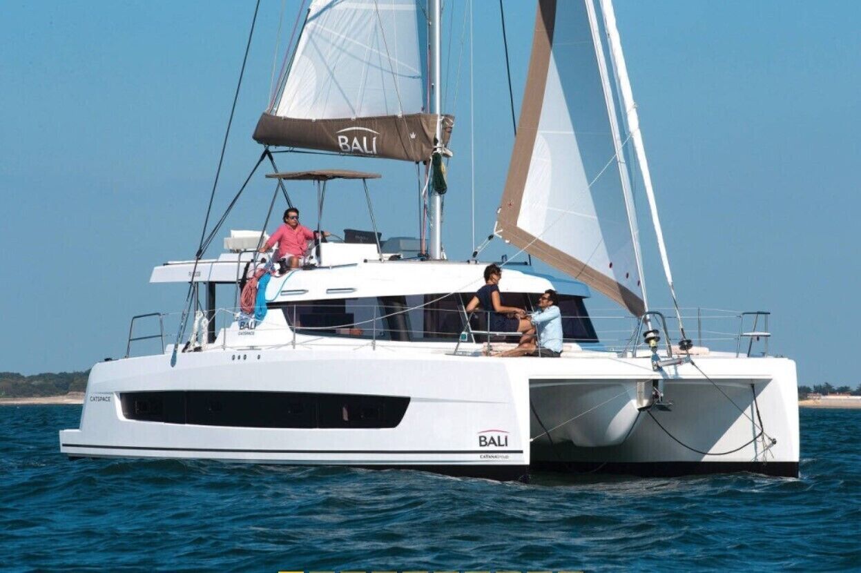 En vit yacht med texten ”BALI” på skrovet, en hytt och ett segel.