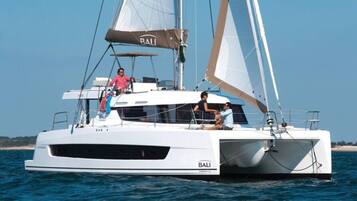 En vit yacht med texten ”BALI” på skrovet, en hytt och ett segel.