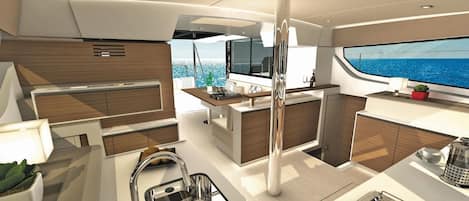 Ein modernes Yachten-Interieur mit einer zentralen Küchenzeile, einem Essbereich und einem großen Fenster mit Blick aufs Meer.