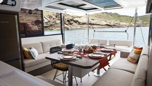 A boat interior with a dining area, seating, and a view of the water. - Caribbean Bliss: Sun-soaked Sailing Adventure from San Vicente y las Granadinas (Ribishi)