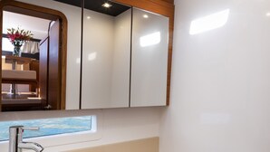 A bathroom with a glass sink, wooden cabinets, a mirror, and a window. - Sun-Kissed Sailing Adventure in Sibenik, Croatia (Primošten)
