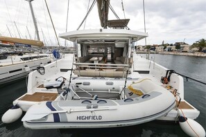 Eine Yacht namens 'HIGHFIELD' liegt in einer Marina vor Anker, mit einem überdachten Sitzbereich, einem kleinen Deck und einem Schild mit der Aufschrift 'HOLIDAY INN'.