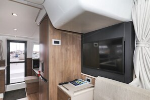 Ein kompaktes Wohnmobil-Interieur mit Fernseher, einem kleinen Tisch mit Fernbedienung und einem Fenster mit Ausblick.