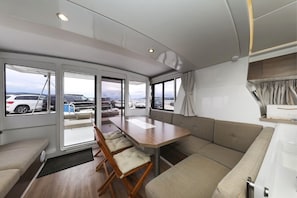 Ein modernes Wohnmobil-Interieur mit Essbereich, Sitzgelegenheiten und großen Fenstern, die einen Blick auf geparkte Autos und einen bewölkten Himmel bieten.
