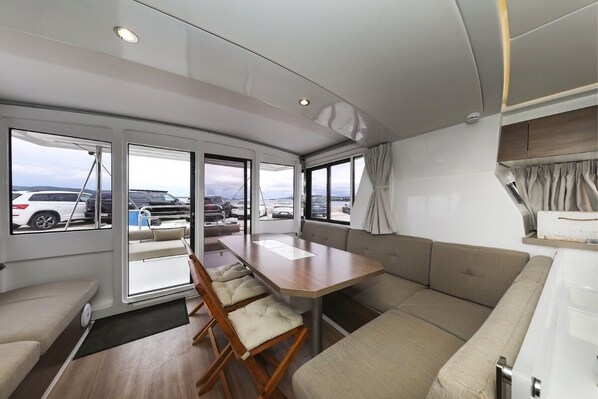 A modern RV interior with a dining area, seating, and large windows offering views of parked cars and a cloudy sky. - Sun-Kissed Sailing Adventure in Zadar, Croatia (Biograd na moru)