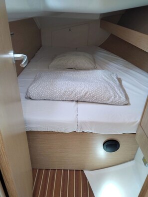 Eine kleine Holzhütte mit einem Einzelbett, Holzboden, einem kleinen runden Lüftungsventil und einer weißen Bettdecke.
