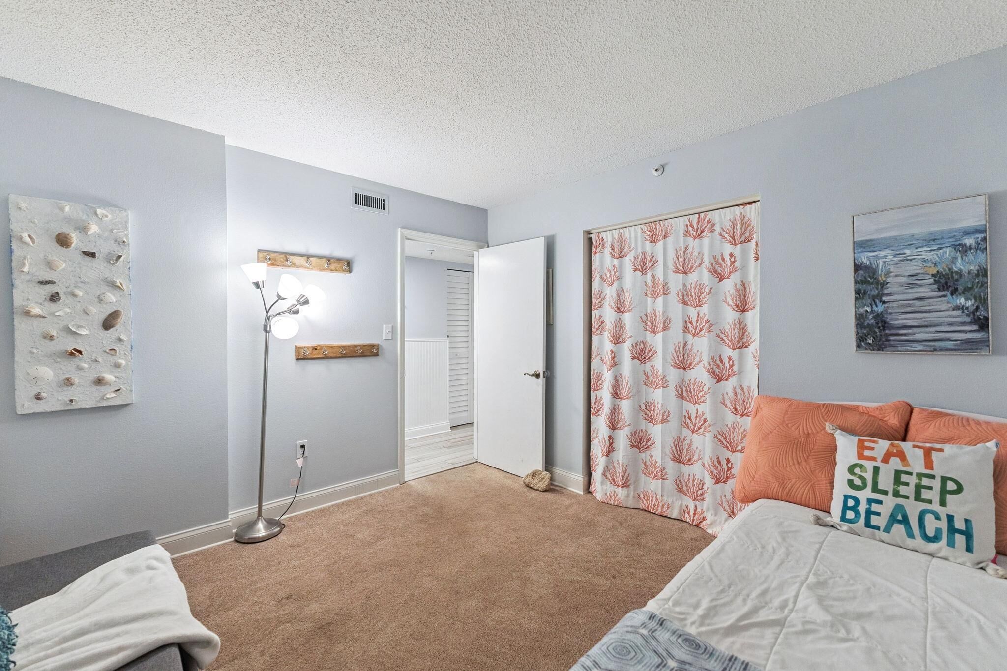 A bedroom with a bed, a floor lamp, a door, and a wall with a painting.