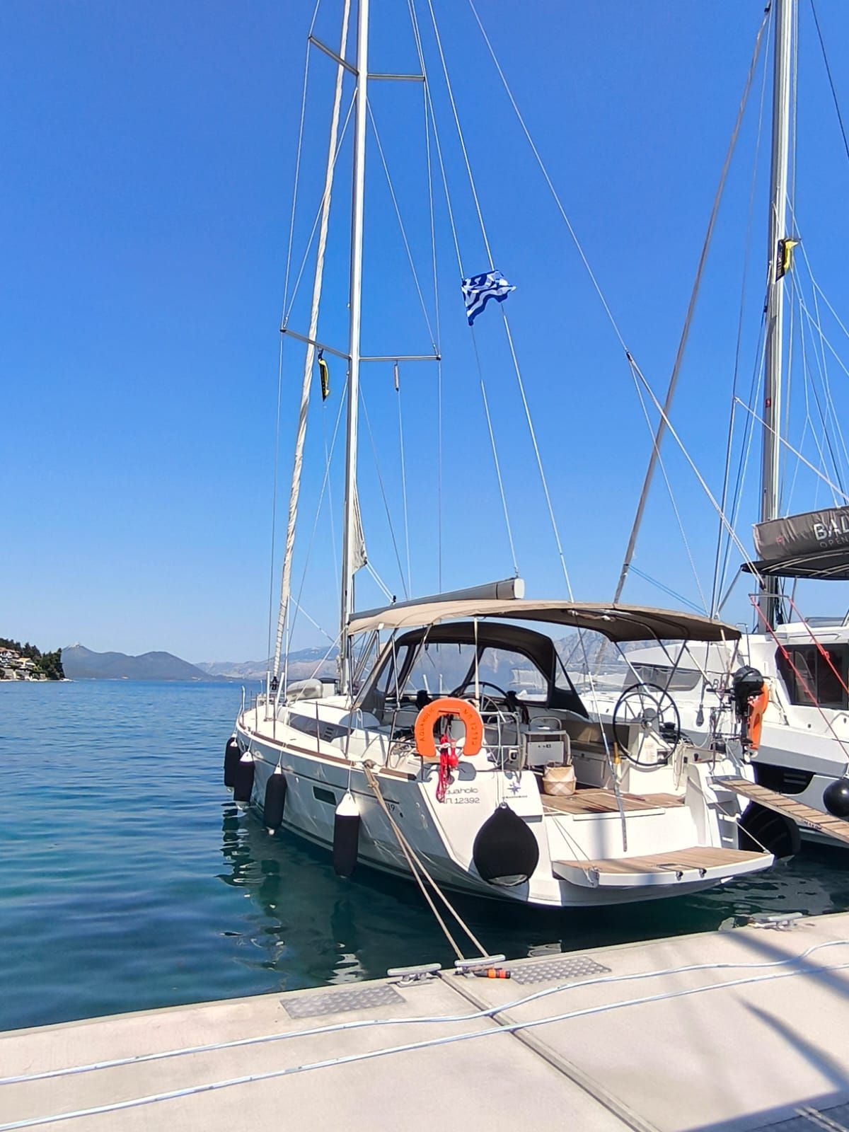 Eine Segelyacht liegt in einer Marina, der Himmel ist klar und das Wasser ruhig.