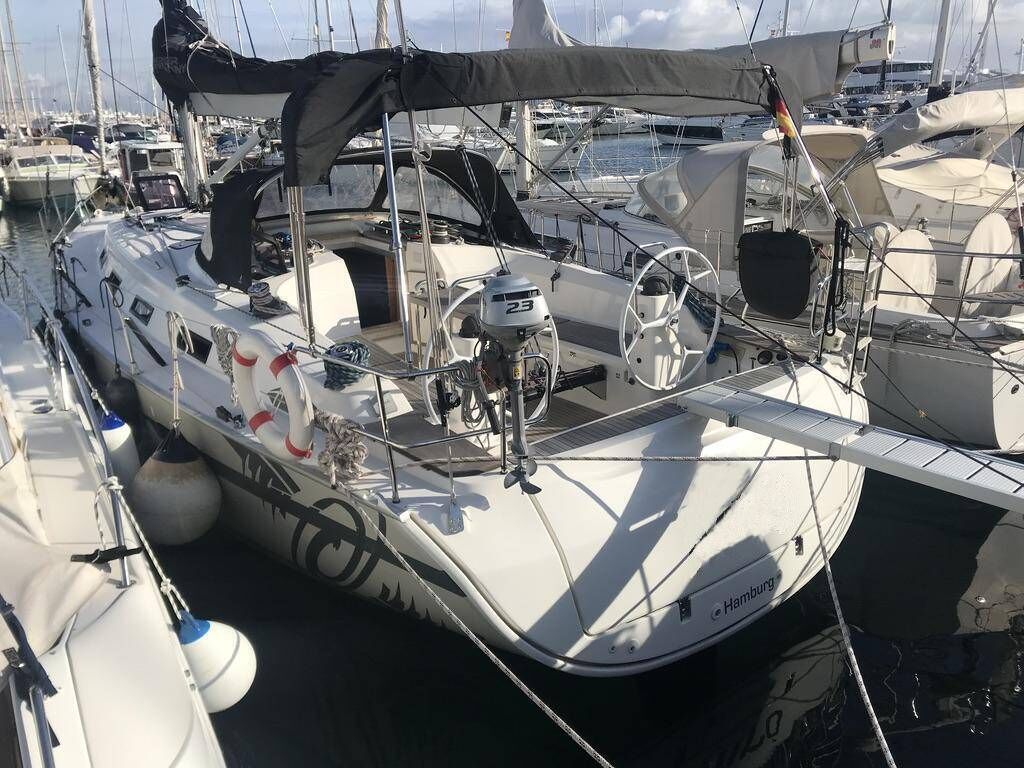 Un velero amarrado en un puerto deportivo con cubierta techada, un timón y un cabrestante.