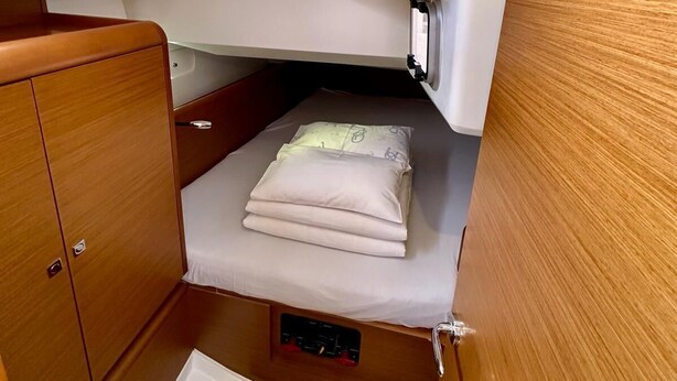 Uma cabine compacta com beliche, uma pequena janela e um armário de madeira.
