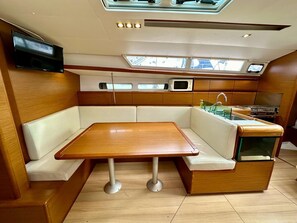 A compact kitchen with a wooden table, white cushioned seating, a microwave, and a stove. - Sun-Kissed Sailing Adventure in Zadar, Croatia (Bibinje)