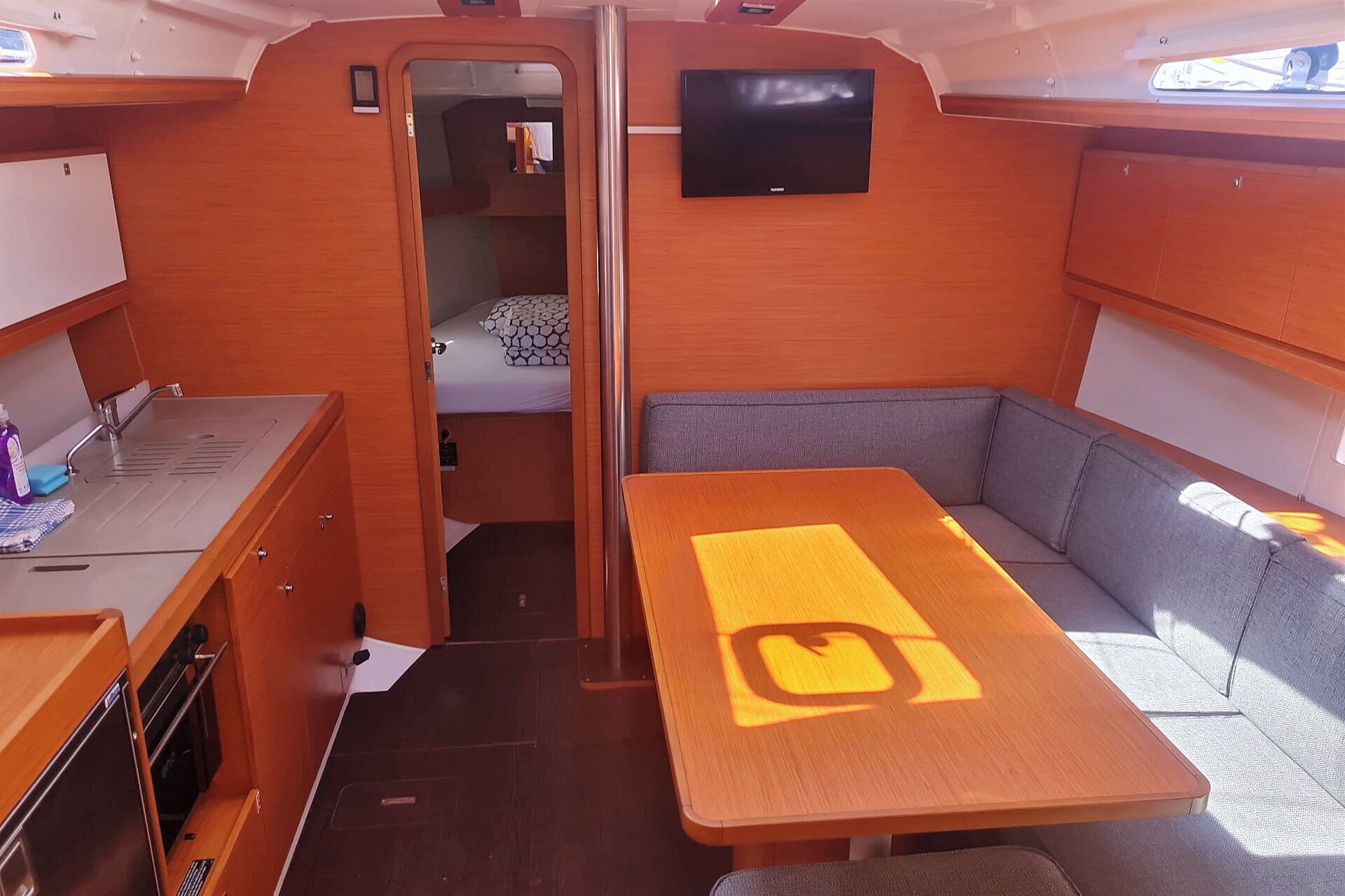 Een compact camperinterieur met een kitchenette, een bed, een zithoek en een televisie.