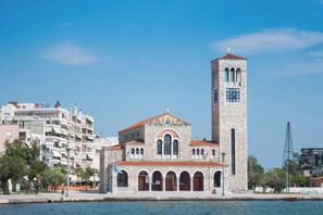 Uma igreja com uma alta torre do sino e um relógio, cercada por edifícios modernos e uma orla marítima.