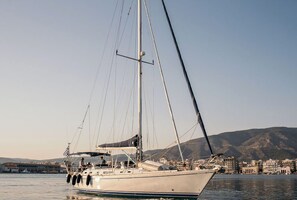 Eine Segelyacht liegt in einer Marina vor der Kulisse von Gebäuden und Hügeln.