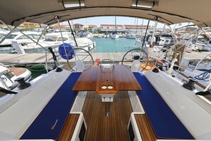 A boat deck with a wooden table, blue cushions, and a view of a marina with other boats. - Sibenik Sun-soaked Sailing: A Luxurious Croatian Voyage (Pirovac)