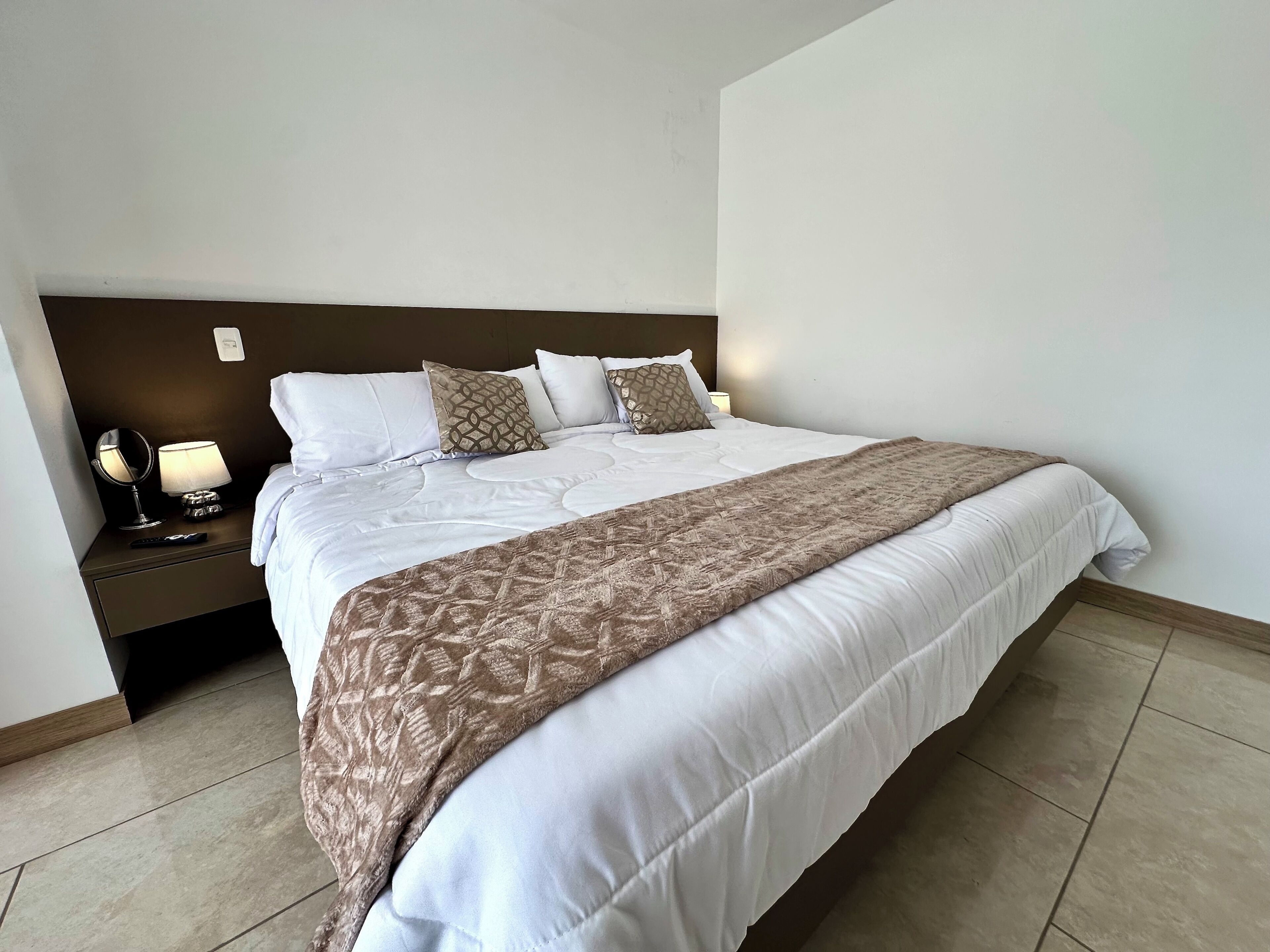 A neatly made bed with a patterned throw, a bedside lamp, and a remote control on the nightstand.
