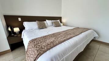 A neatly made bed with a patterned throw, a bedside lamp, and a remote control on the nightstand.