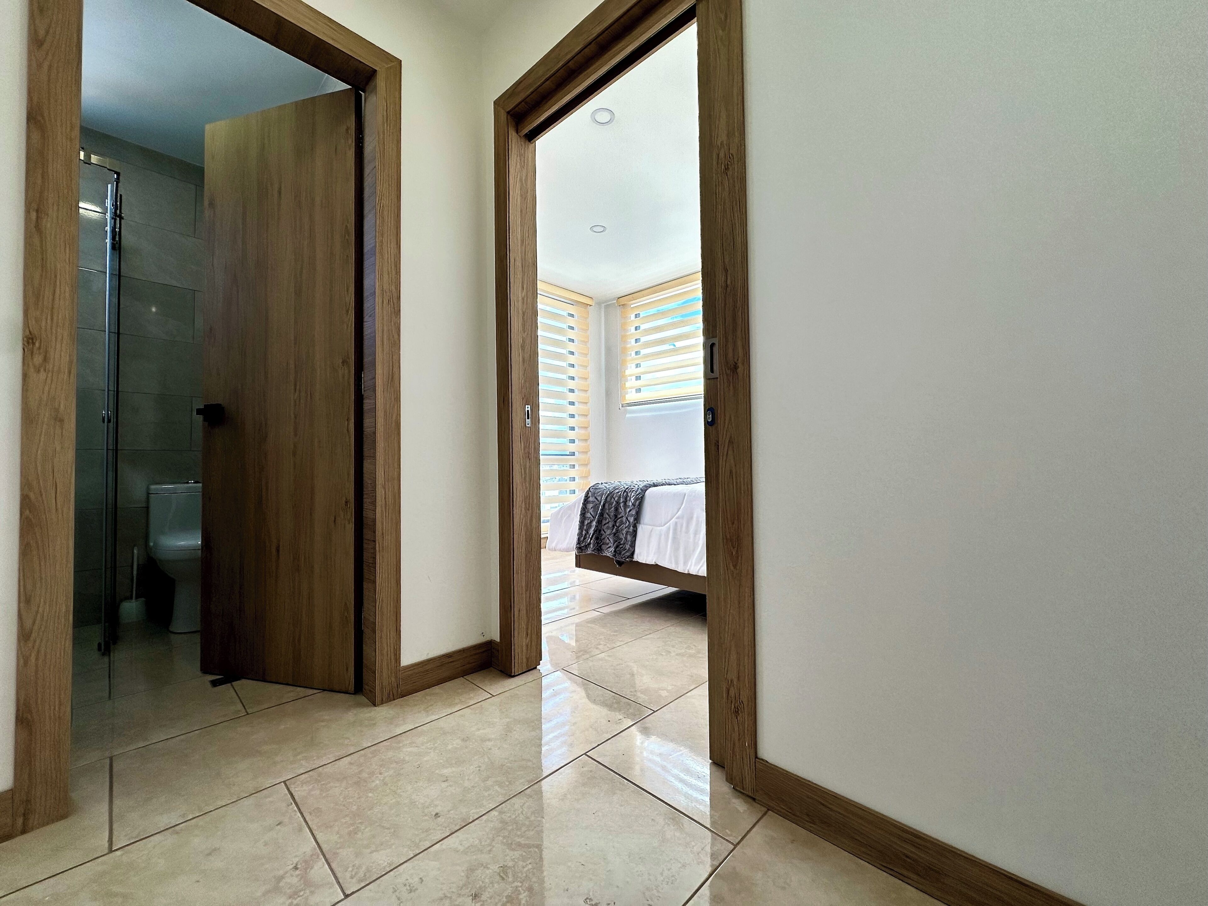 Un pasillo con una puerta de madera que da a un baño y un dormitorio.