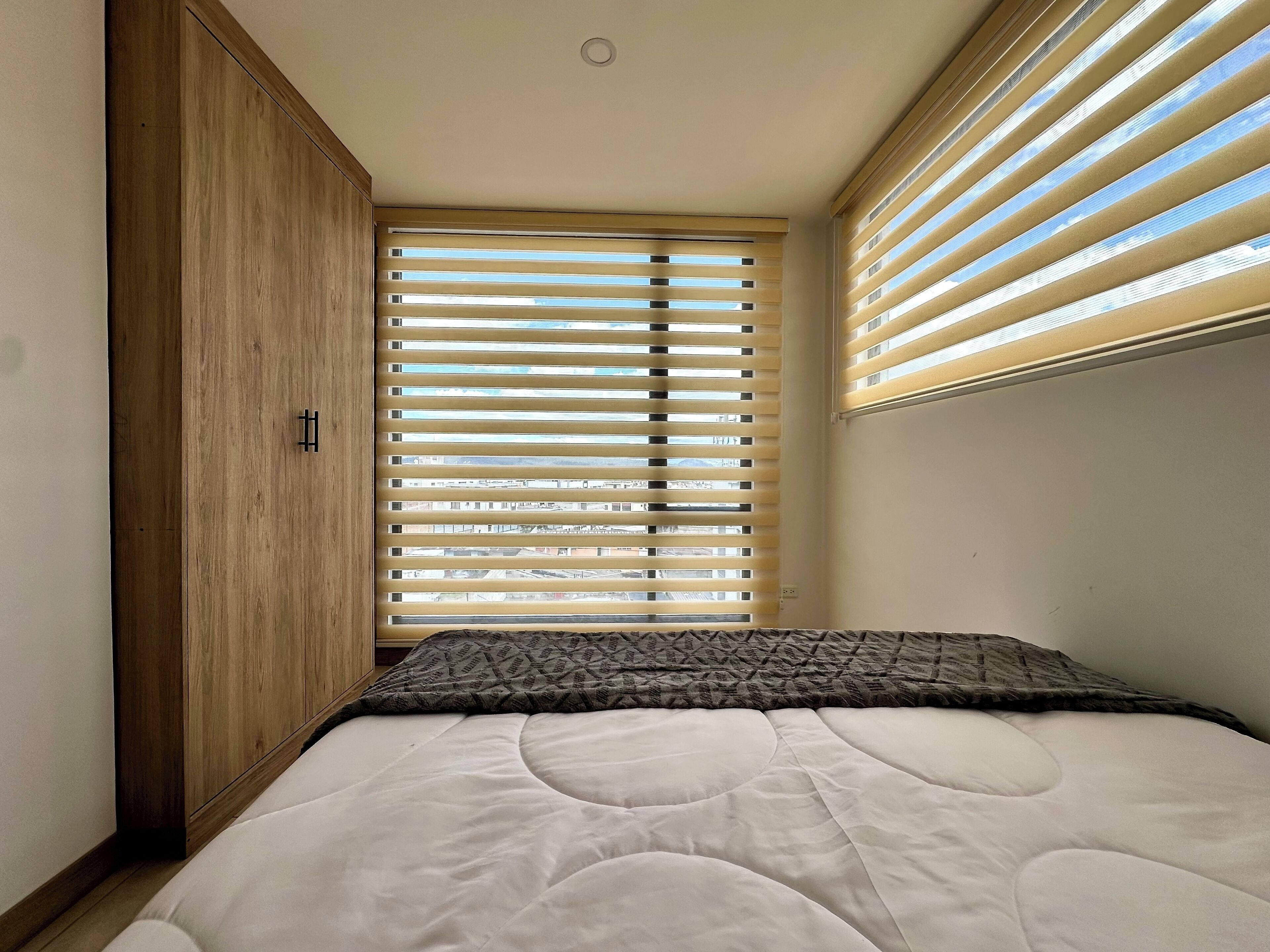 A bedroom with a bed, a wardrobe, and a window with blinds.