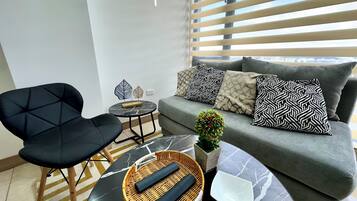 Una sala moderna con un sofá, un sillón negro, una mesa redonda y cojines decorativos.