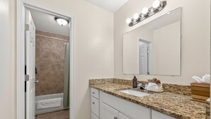 A bathroom with a shower, sink, vanity, and a mirror with lights.