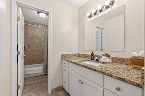 A bathroom with a shower, sink, vanity, and a mirror with lights.