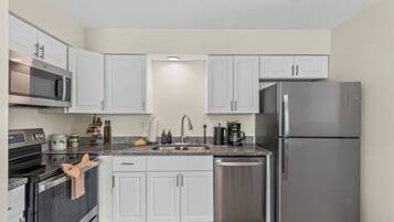 A kitchen with white cabinets, stainless steel appliances, a granite countertop, and a dishwasher.