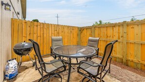 A patio with a round table and four chairs, a barbecue grill, and a bag of charcoal.