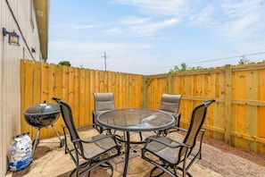 A patio with a round table and four chairs, a barbecue grill, and a bag of charcoal.
