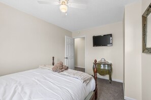 A bedroom with a bed, a dresser, a ceiling fan, and a television on the wall.