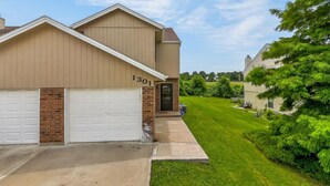 A residential building with two garage doors, a brick entrance, and a well-maintained lawn.