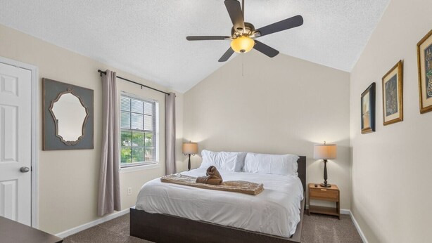 A bedroom with a bed, two bedside tables, a ceiling fan, a window with blinds, and a door.