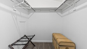 A small, white-walled room with a slanted ceiling, a metal rack, a brown suitcase, and a carpeted floor. - Remote Work Ready | 3BR | Google Fiber | Kings (Lee`s Summit)