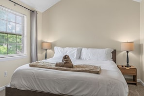 A neatly made bed with white linens, two bedside lamps, and a window with blinds.