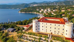 A castle with a red roof, surrounded by greenery and a body of water. - Sun-Kissed Sailing Adventure in Northern Croatia (Kraljevica)